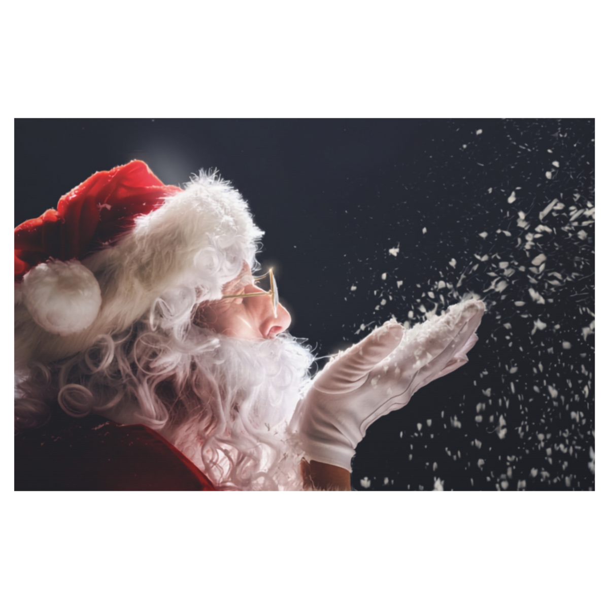 A festive holiday photo print of Santa Claus in profile, wearing his classic red hat with white fur trim and white gloves, blowing snow towards the right against a dark background.